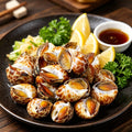 Spotted babylon snails plated with lemon wedges and fresh herbs