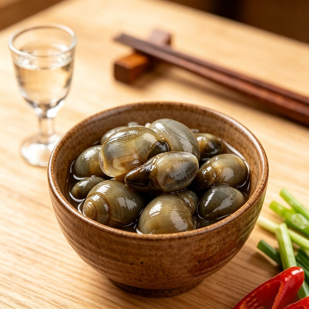 Marinated shellfish in a small bowl set beside chopsticks and a glass of water